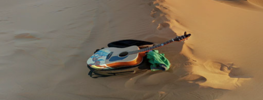 Travel acoustic guitar resting on sand dunes, symbolizing creativity and music on the road in remote landscapes.
