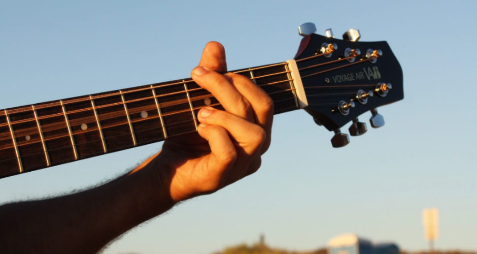 A musician playing a Voyage Air guitar at sunset, close-up of the fretboard and headstock outdoors.