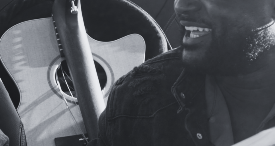 Travel folding acoustic guitar inside a car with musician smiling, highlighting compact guitar storage for musicians on the go.