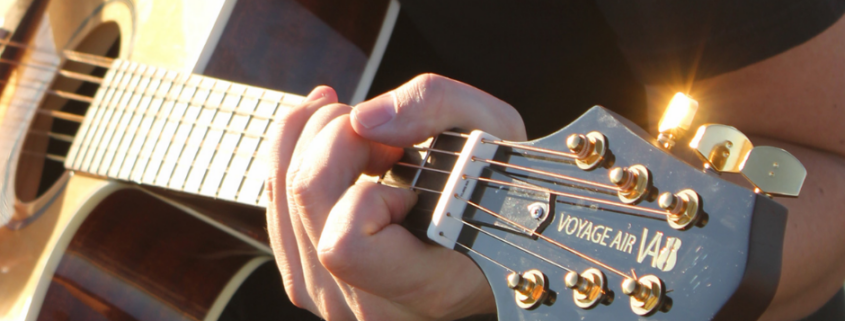Close-up of a guitarist playing a Voyage Air folding acoustic guitar, highlighting the instrument’s compact, travel-ready headstock and quality craftsmanship.